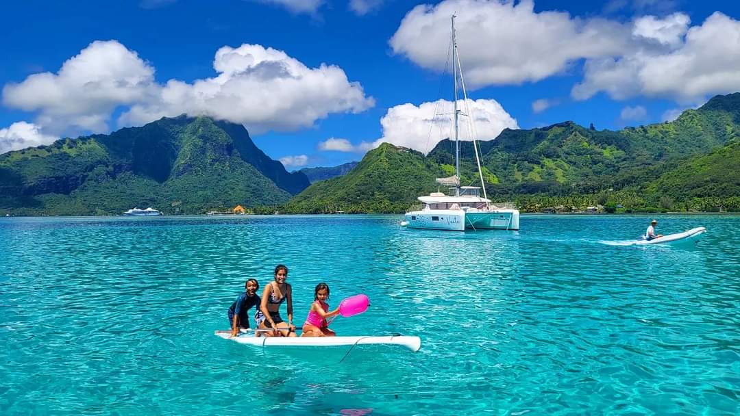 Family Paddleboarding near a private catamaran Catamaran sailing near Bora Bora overwater bungalows