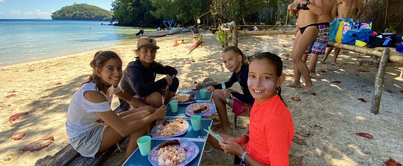 A smiling family on the the beach enjoying a bbq in a turquoise lagoon