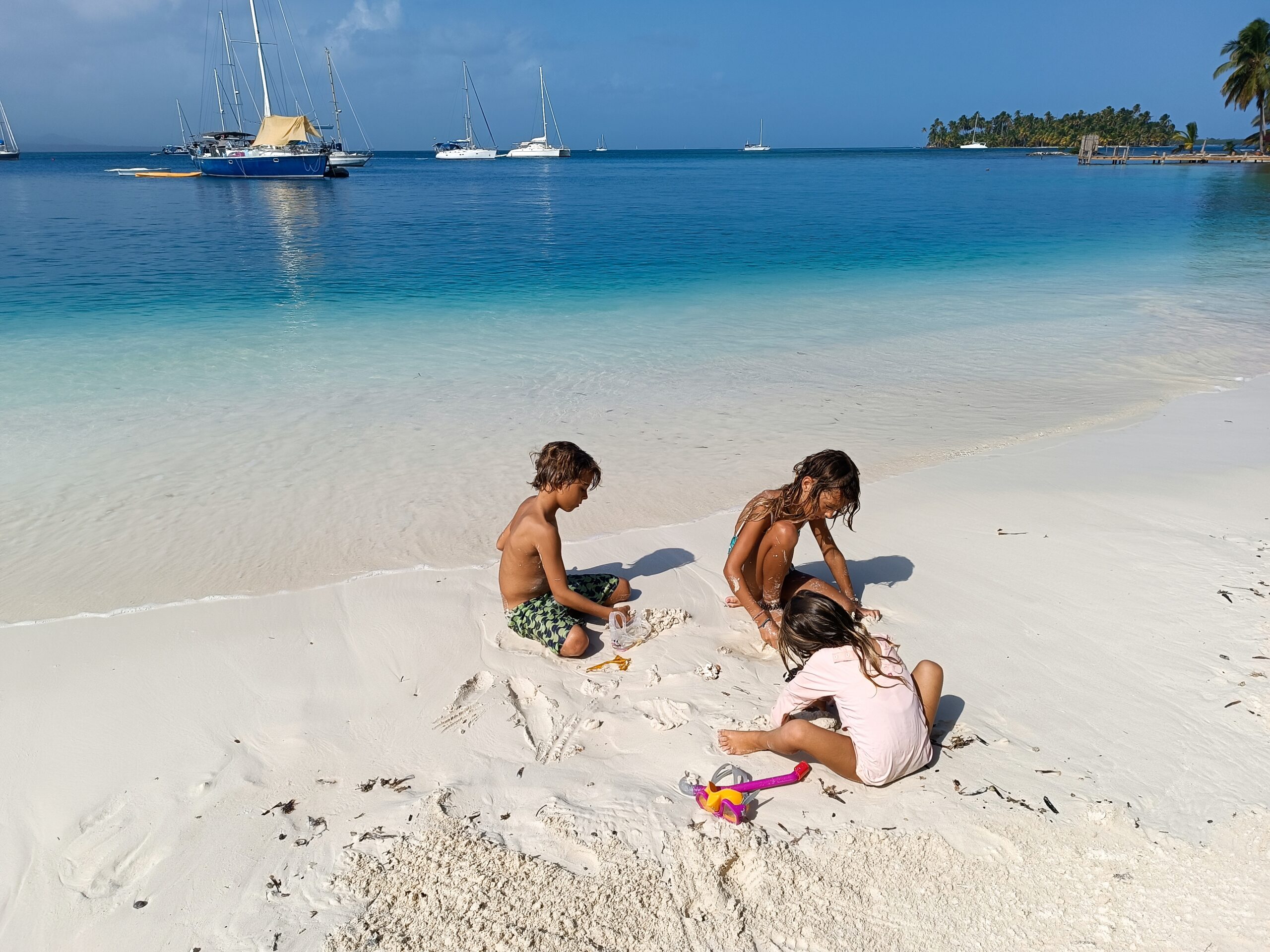 Children playing on white-sand beach near catamaran in Bora Bora