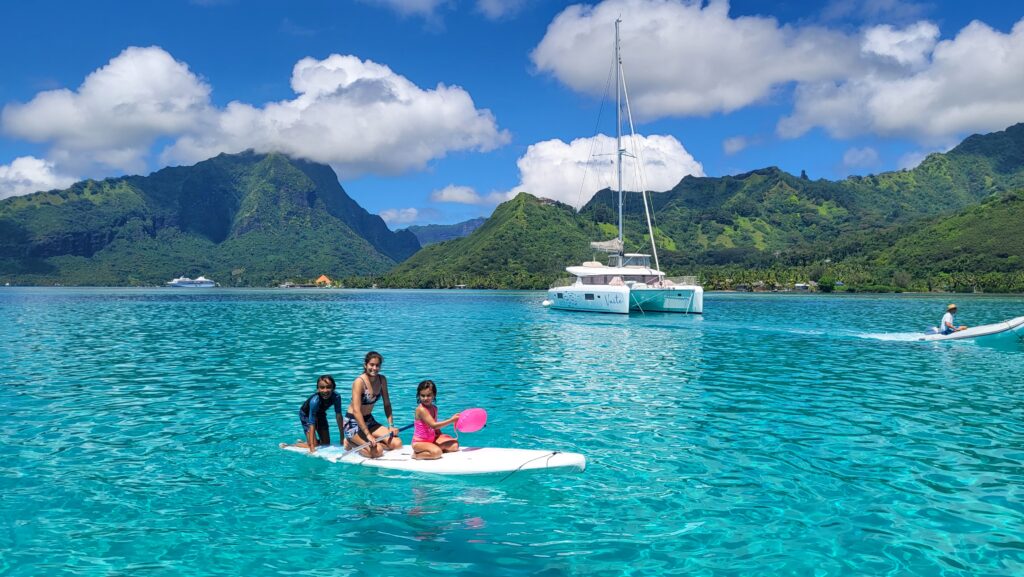 Family paddle boarding in the lagoon between Tahiti and Moorea during a catamaran cruise