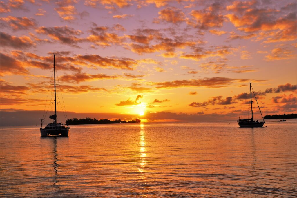 Catamaran and sailing yacht at anchor during sunset in the Tuamotu Islands lagoon
