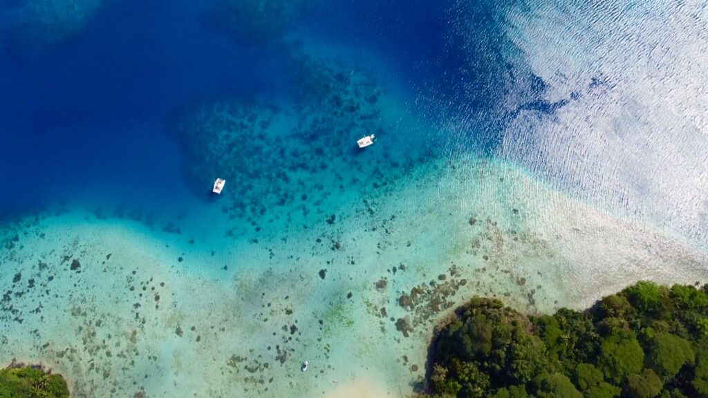 Aerial view of catamarans anchored in the turquoise lagoon of Huahine in the Leeward Islands of French Polynesia.